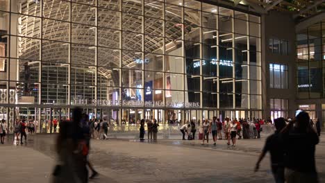 Timelapse-shot-at-the-front-entrance-of-The-Shoppes-at-Marina-Bay-Sands,-capturing-the-exterior-and-large-crowds-of-people-entering-and-existing-the-shopping-centre-at-night,-downtown-Singapore