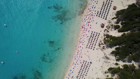 Cala-agulla-beach-with-turquoise-waters-and-vibrant-beachgoers-on-sunny-day,-close-up,-aerial-view