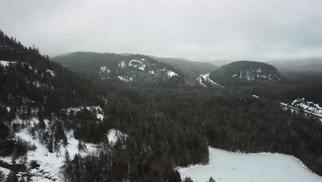 Una-Toma-Aérea-De-Montañas-En-Los-Adirondacks-Con-El-Bosque-Y-Un-Lago-Congelado