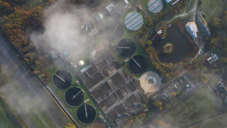 Sewage-water-treatment-plant-aerial-view-looking-down-through-clouds-at-waste-quality-control-tanks