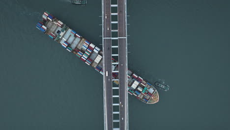 Large-freight-ship-passing-under-suspension-bridge-High-altitude-top-down-drone-shot