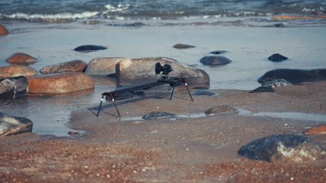 Eine-Kamera-Und-Ein-Slider-Rig,-Die-Am-Sandstrand-Aufgestellt-Sind-Und-Die-Wellen-Filmen,-Die-Auf-Die-Felsen-Zurollen