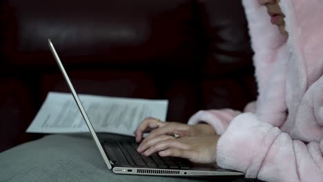 Person-in-pink-robe-typing-on-laptop,-seated-indoors,-concept-of-work-from-home,-low-light,-cozy-atmosphere