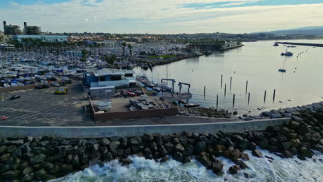 Ein-Geschäftiger-Yachthafen-Im-Morgengrauen-Mit-Angedockten-Booten-Und-Der-Skyline-Der-Stadt-Im-Hintergrund,-Ruhiges-Wasser,-Luftaufnahme