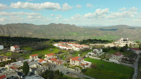 Aerial-panoramic-aerial-view-of-Lefkara,-Cyprus,-traditional-architecture-with-red-tiled-roofs,-interspersed-with-greenery-and-set-against-the-backdrop-of-rolling-hills-and-mountains