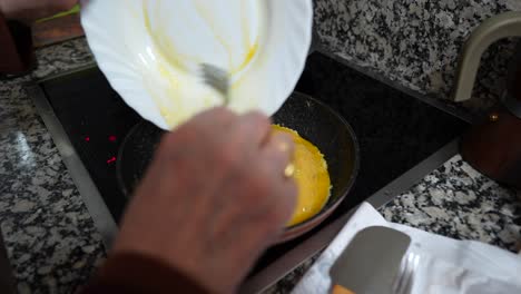 Granny-pouring-beaten-egg-into-a-frying-pan-to-cook-an-omelette