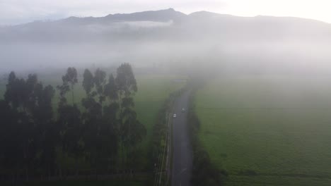 Vuelo-De-Drones-Sobre-El-Coche-La-Carretera-En-Una-Espesa-Niebla-En-Una-Gran-Zona-De-Pastizales-Con-Colinas-En-El-Fondo