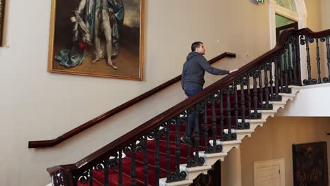 Young-man-walks-on-old-fashioned-stairs-with-artistic-paintings-in-background-inside-Dublin-Castle