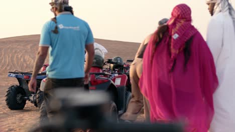 Group-of-people-preparing-for-a-quad-bike-adventure-in-Dubai-desert,-sunlit-dunes