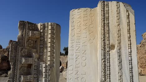 Antike-Römische-Säulenruinen-Mit-Gravuren-Unter-Blauem-Himmel-In-Karthago,-Tunesien