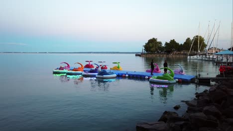 Rentable,-colorful,-illuminated-and-modern-pedal-boats-on-the-calm-lake-at-early-evening-in-Balatonfured,-Hungary