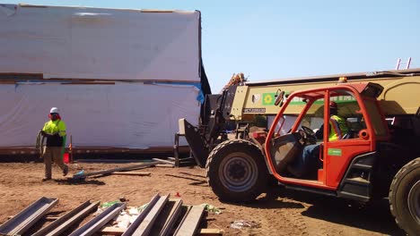 Gimbal-panning-shot-of-industrial-fork-lift-backing-up-at-a-pre-fab-housing-construction-site-in-West-Los-Angeles,-California