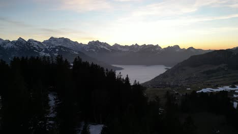 Amden-Weesen-Switzerland-flight-over-silhouetted-forest-as-sun-leaves-the-valley