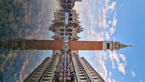 Basilica-and-Campanile-reflect-in-flooded-Piazza-San-Marco,-tourists-stroll-alongside