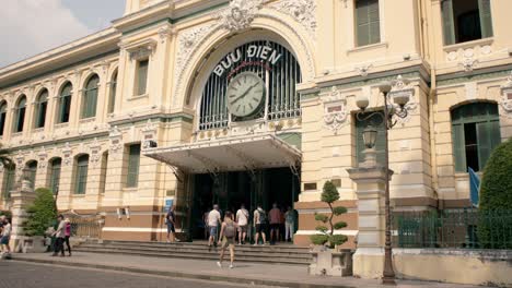 People-walking-in-front-of-Saigon-Central-Post-Office-in-Vietnam,-sunny-day