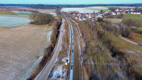 Luftaufnahme-Eines-Zuges,-Der-Inmitten-Des-Schmelzenden-Winterschnees-Am-Dorf-Vorbeigleitet