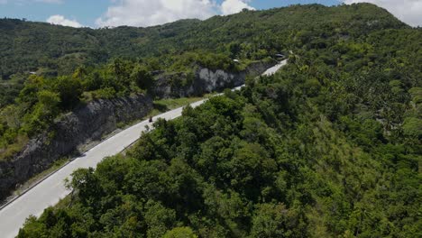 Un-Camino-Sinuoso-En-La-Isla-De-Cebú-Con-Exuberante-Vegetación-Y-Scooters-En-Movimiento,-Vista-Aérea