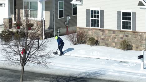 Person-with-yellow-hat,-snow-shoveling-on-sidewalk-during-winter