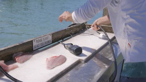 Mann-Spritzt-Einen-Fischschneidetisch-Mit-Wasser-Aus-Einem-Schlauch-Auf-Einem-Dock-In-Florida-Ab