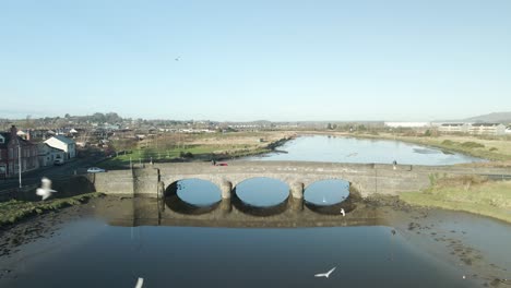Three-arch-stone-bridge-over-Castlebridge-River-in-Dundalk,-Ireland-with-birds-flying,-clear-day