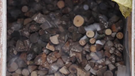 timber-firewood-stash-outside-during-winter-time,-snow-is-falling,-shallow-depth-of-field,-handheld-slowmotion