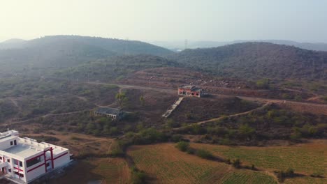 Toma-Aérea-De-Un-Dron-De-Un-Edificio-Abandonado-De-Una-Estación-De-Tren-Con-Un-Paisaje-Montañoso-De-Aldea-Al-Fondo-En-Madhya-Pradesh,-India