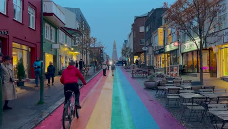 Cyclist-on-Rainbow-Street-in-Reykjavik-at-dusk,-vibrant-city-life-with-soft-lighting