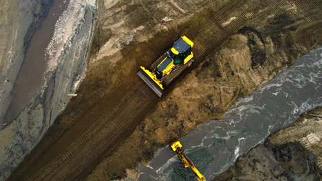 Una-Topadora-Que-Gestiona-La-Sedimentación-Y-El-Desvío-De-Estanques-En-Una-Zona-Industrial,-Luz-Del-Día,-Vista-Aérea