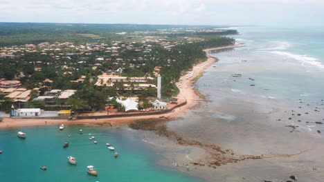 Aerial-view-of-Praia-do-Forte-beach,-the-coral-reef,-boats-parked,-palm-tree-area-on-a-cloudy-day,-Praia-do-Forte,-Bahia,-Brazil