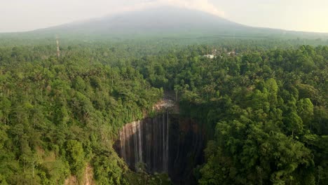 Erleben-Sie-Die-Atemberaubende-Synergie-Der-Natur:-Die-Drohnenperspektive-Fängt-Einen-Majestätischen-Wasserfall-Ein,-Der-In-Einer-Dschungeloase-Eingebettet-Ist,-Mit-Einem-Hoch-Aufragenden-Vulkan,-Der-Die-Kulisse-In-Ehrfurchtgebietender-Erhabenheit-Malt