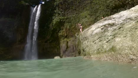 Person-leaping-off-cliff-into-serene-water-at-a-waterfall-in-the-Philippines,-daylight