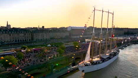 Four-mast-sailing-ships-in-the-Garonne-River-during-Wine-Fair-with-large-crowds,-Aerial-dolly-out-reveal-shot