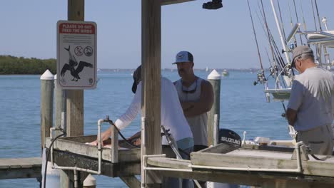 Men-cutting-fish-at-cleaning-station-on-dock-and-throwing-scraps-into-ocean-to-pelicans-with-no-feeding-sign-in-Florida