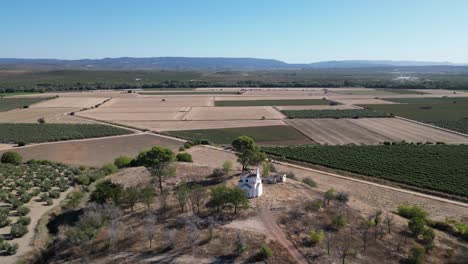 The-aerial-grace-of-La-Ermita-del-Poblado-de-San-Julián-in-Spain,-an-enduring-emblem-of-spiritual-dedication-in-Marmolejo,-framed-by-the-scenic-beauty-of-Spain's-agricultural-fields