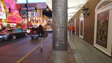 Incline-La-Vista-Desde-El-Pavimento-Para-Revelar-Una-Turista-Caminando-Junto-A-Una-Farola-Con-Un-Cartel-Que-Dice-&quot;Experiencia-En-La-Calle-Fremont-En-Las-Vegas&quot;