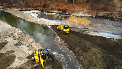 Excavators-manage-sediment-in-a-pond,-aerial-view,-construction-in-natural-setting