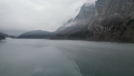 Klöntalersee-Glarus-Switzerland-slow-and-smooth-low-flight-along-misty-Swiss-Alp-lake