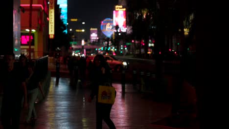 Happy-young-woman-with-shopping-bag-walks-down-sidewalk-at-night-on-the-Las-Vegas-strip