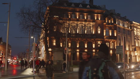 Twilight-cityscape-with-illuminated-historic-building,-blurred-pedestrians,-Dublin