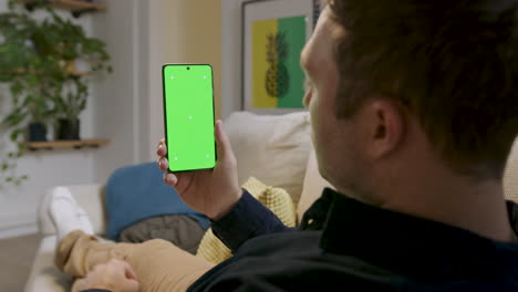 Detail-of-a-man-touching-his-cell-phone-screen-in-Choma-Key-sitting-on-the-sofa-in-his-home