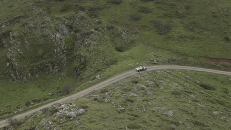 People-on-board-of-convertible-vintage-car-driving-along-narrow-and-winding-mountain-road,-Basque-Pyrenees,-Col-Inharpu-in-France