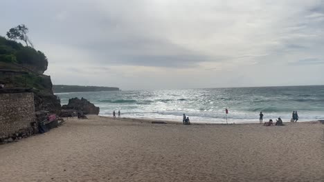 Cámara-Pegando-En-Una-Playa-Ventosa-En-Bali-En-La-Temporada-De-Lluvias-Mientras-La-Gente-Camina