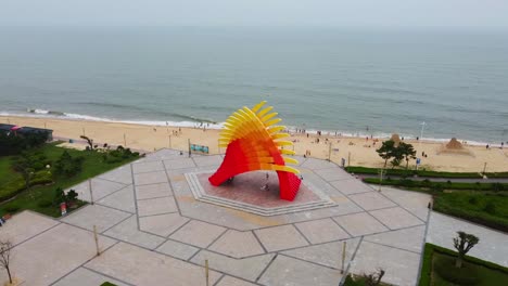 A-vibrant-beach-sculpture-and-the-shore-in-Nanhai-beach-park-China-on-an-overcast-day,-aerial-view