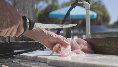 Man-cutting-fish-meat-on-cleaning-table-on-a-dock-near-his-boat-in-Florida