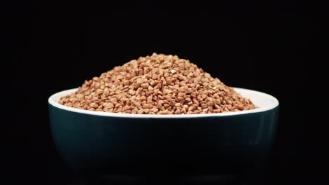 Close-up-of-the-buckwheat-grains-on-the-blue-bowl-rotating-on-the-black-background