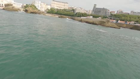 Freestyle-drone-flying-at-low-altitude-around-rocks-of-Port-des-Pecheurs-or-Fisherman-Port-with-city-in-background,-Biarritz-in-France