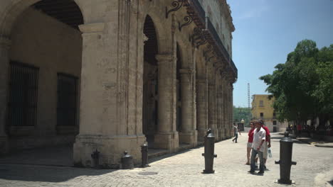 From-a-distinctive-perspective-of-Plaza-Vieja,-one-can-catch-sight-of-the-Havana-Cathedral,-while-some-tourists-leisurely-walks,-admiring-the-architectural-beauty
