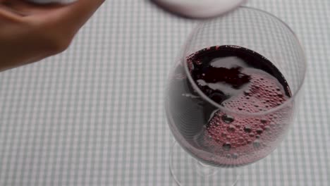 Red-wine-pouring-into-glass,-dynamic-splash,-close-up,-against-checkered-background,-indoors,-selective-focus