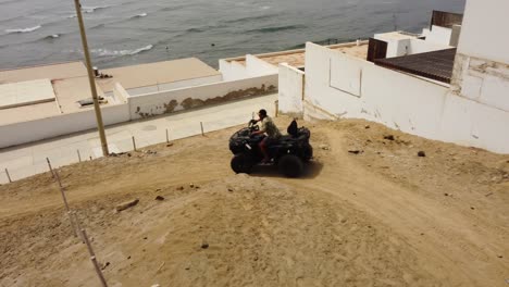 Aerial-shot-of-a-person-riding-an-ATV-or-a-4-wheeler,-going-dirt-path-in-an-sea-side-town