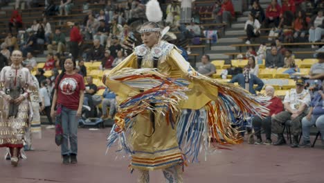 A-spirited-female-traditional-Native-American-dancer-dressed-in-yellow-regalia-competes-in-the-dance-competition-at-an-indoor-Powwow